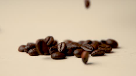 Roasted-coffee-beans-fall-from-above-on-a-beige-surface-slow-motion-vintage-look