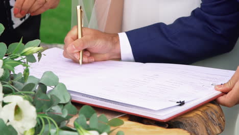 Novio-Con-Traje-Azul-Firmando-Un-Certificado-De-Matrimonio-Con-Un-Bolígrafo-Dorado