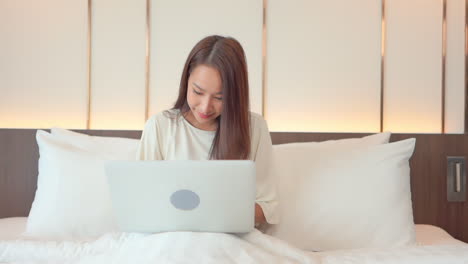 Why-work-from-home-when-you-can-work-from-anywhere,-woman-types-on-her-laptop-as-she-sits-up-in-bed