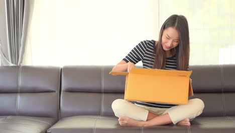 Asian-young-woman-happily-opens-yellow-post-box-and-showing-happy-face-expression-while-sitting-on-a-couch-daytime