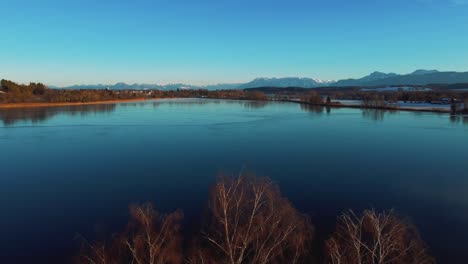4K-UHD-aerial-drone-flight-moving-forwards-above-an-icy-frozen-lake-and-tree-tops-in-Bavaria-close-to-the-Alps-in-winter-in-Germany-near-Austria