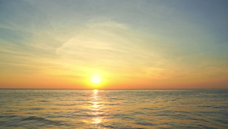 A-huge-yellow-sun-on-the-ocean-horizon-the-sunset-sky-is-pink,-orange,-yellow,-and-blue
