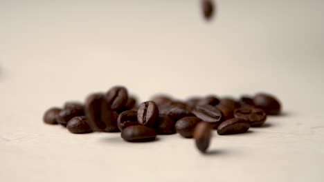 Roasted-coffee-beans-fall-from-above-on-a-beige-surface-slow-motion