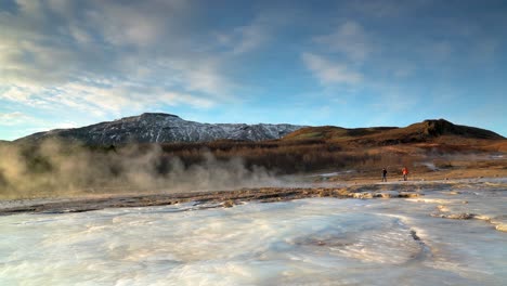 Dos-Personas-Esperando-La-Erupción-De-Strokkur-En-El-área-Geotérmica-De-Haukadalsvegur,-Islandia