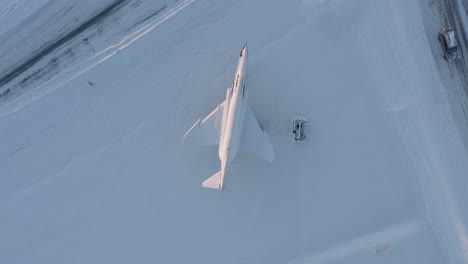 Directly-above-inactive-fighter-jet-with-snow-as-memorial-in-Keflavik,-Iceland