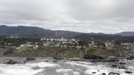 Brookings-city-on-rugged-Oregon-coastline,-houses-on-clifftop,-aerial-rising