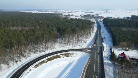 Car-Drives-Down-The-Highway-During-Sunny-Day-In-Rakowice,-Krakow,-Poland-With-Snow-Covered-Woodland-On-The-Background