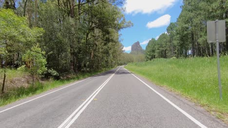 Rear-facing-driving-point-of-view-POV-of-a-deserted-Queensland-country-road-with-dramatic-Mount-Coonowrin-framed-by-trees---ideal-for-interior-car-scene-green-screen-replacement