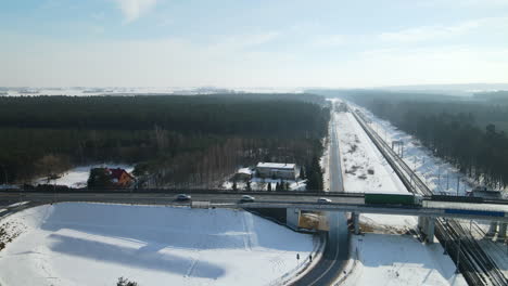 Vehicles-Passing-By-The-Bridge-Over-Empty-Railway-In-Rakowice,-Krakow,-Poland-With-Snow-covered-Urban-Landscape-In-Winter
