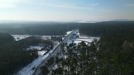 Aerial-view-of-traffic-on-polish-autostrada-surrounded-by-pine-tree-forest-during-sunny-day-in-winter