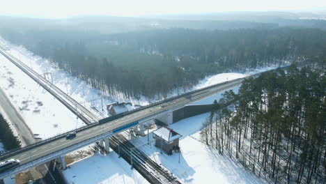 Aerial-shot-of-driving-cars-on-bridge-over-railroad-line-during-winter-and-sunlight