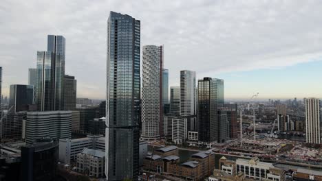 Aerial-shot-of-birds-flying-in-front-of-gigantic-modern-skyline-in-London-during-cloudy-day-early-in-the-morning