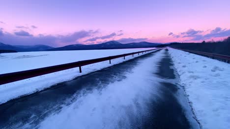 Snow-blowing-across-a-beautiful-promenade-over-a-frozen-lake-during-winter-with-mountains-in-the-background-during-sunset-in-the-Appalachian-mountains