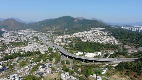 Aerial-view-of-Hong-Kong-outskirts-residential-area,-with-connecting-highway-and-surrounding-mountain-slopes