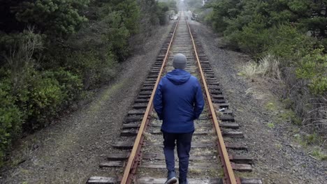 Back-view-of-man-walking-alone-on-railroad-tracks