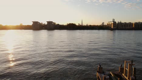 Luftüberführung-über-Die-Themse-Bei-Sonnenuntergang-Mit-Wasserreflexion,-Kreuzfahrtschiff-Und-Skyline-Silhouette