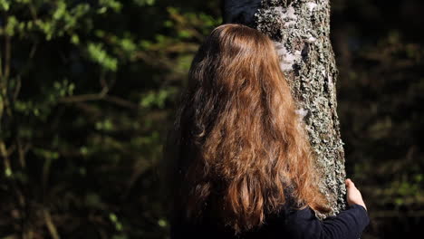 Woman-with-long-brown-hair-hugging-tree,-looking-up-smiling
