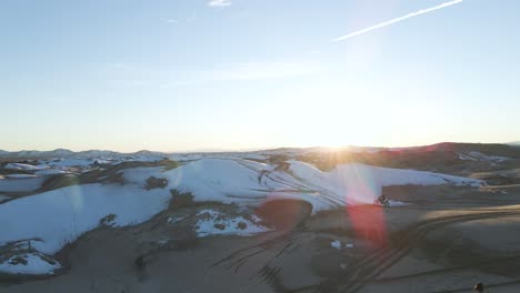 Aerial-view-of-riding-motocross-bike-on-sand-dunes-covered-with-snow,-Little-Sahara,-Utah