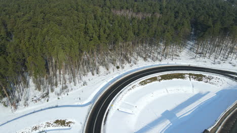 Schneebedeckte-Straßen,-Lastwagen-Und-Autos,-Die-Sich-Entlang-Der-Autobahn-In-Einer-Winterwaldlandschaft-In-Rakowice-Polen-Bewegen---Luftdrohne,-Die-Von-Einem-Festen-Punkt-Aus-Nach-Rechts-Schwenkt