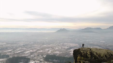 Two-people-standing-on-a-rock-overlooking-the-city-bellow