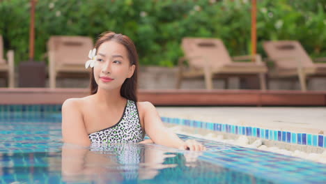Beautiful-young-asian-female-model-in-swimsuit-and-hair-flower-in-swimming-pool-of-luxury-tropical-hotel