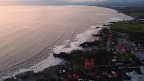 drone-fly-above-tanah-lot-hinduist-temple-in-bali-indonesia-island-of-Gods,-tradition-and-ceremony,-ocean-seascape-view-during-stunning-sunset