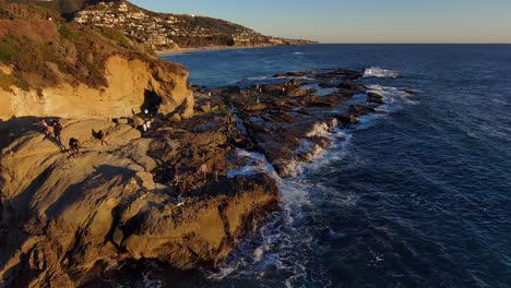 Aerial-drone-view-of-people-exploring-an-ocean-front-rock-formations-in-Laguna-Beach,-California