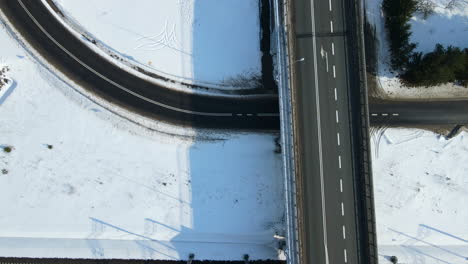 Cars-moving-along-the-Bridge-which-crosses-highway-and-railroad-in-winter-Poland-Rakowice---daytime-drone-top-down-view-slow-motion