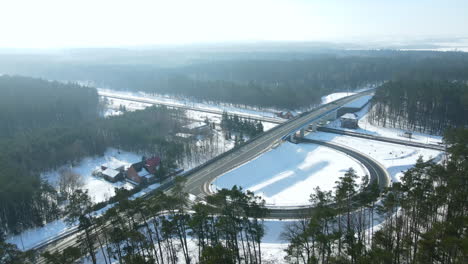 Aerial-orbit-shot-of-snowy-highway-during-winter-and-sun-with-crossing-traffic-and-exit-road