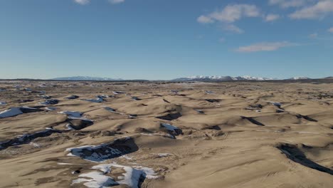 Low-angle-aerial-pan-shot-of-Little-Sahara-Sand-Dunes-covered-with-snow-and-ice-during-sunny-day-and-blue-sky-in-winter
