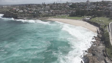 Coastline-With-Buildings,-Cliffs,-And-Ocean-Waves-In-Summer-At-Bronte-Beach-In-Eastern-Suburbs,-Sydney,-New-South-Wales,-Australia---aerial-drone-shot