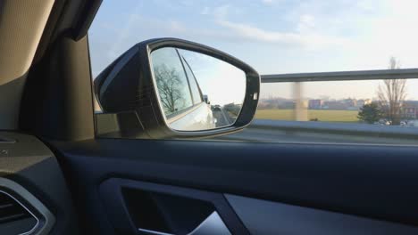 Traveling-on-the-Highway-in-Italy:-view-from-the-Rearview-Mirror,-Cars-following-and-Countryside-and-Panorama-of-the-Padana-Plain-in-the-background---slow-motion