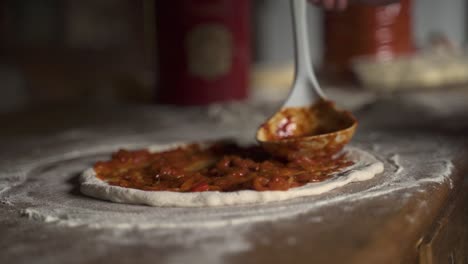 Tomato-sauce-over-raw-home-made-pizza-with-flour-on-wooden-table-Slow-Motion