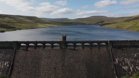 Yorkshire-Scar-house-reservoir-Dam-and-huge-stored-water-amounts-on-clear-sunny-day,-aerial-pan-shot