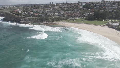 View-Along-The-Foreshore-Of-Bronte-Beach-With-Turquoise-Sea-And-Fine-Sandy-Beach-In-Eastern-Suburbs,-Sydney,-New-South-Wales,-Australia---aerial-drone-shot