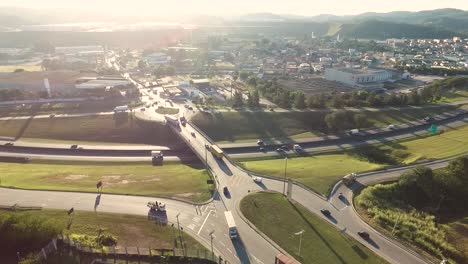 aerial-drone-view-of-large-streets-and-crossroads-with-a-lot-of-traffic-in-the-middle-of-green-areas-and-a-small-city-and-mountains-in-the-background