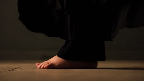 closeup-of-barefoot-feets-with-black-trousers-moving,-turn,-jump-and-dance-on-a-brown-floor
