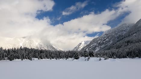 Wide-shot-showing-beautiful-winter-landscape-with-snow-capped-pine-trees-and-cloudscape-between-mountains