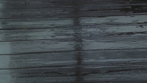 Rain-drops-fall-and-splatter-on-wooden-deck,-close-up