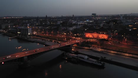 Leaving-Drone-shot-by-night-over-Mainz-right-after-magic-hour-on-a-warm-spring-day-showing-the-city-of-Biontech-in-the-back