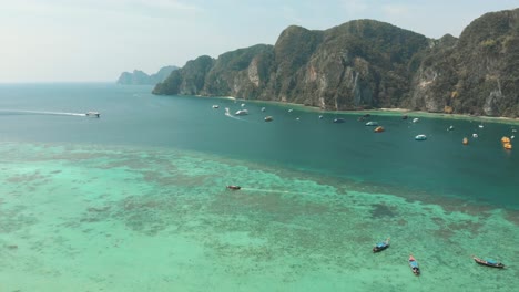 Busy-Harbour-in-Tonsai-Bay-with-Long-tail-boats-and-small-yachts-moored-in-Ko-Phi-Phi-Don-Island,-Thailand---Aerial-Descend-overview-shot