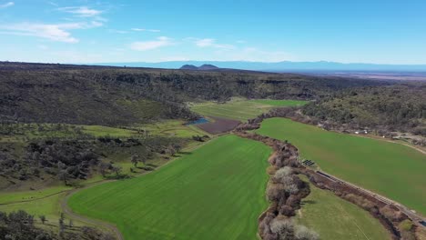 600'-drone-flyover-of-green-valley-lined-with-mountains-and-a-creek-lined-with-trees-running-through-the-middle-of-it