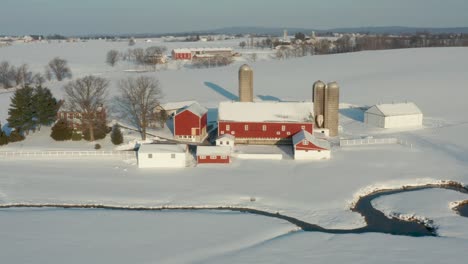 Aerial-of-red-barn-and-farm-buildings-in-winter-snow