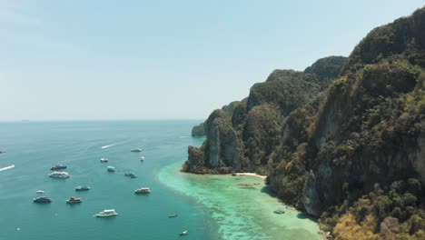 Towering-Limestone-stalled-by-shoreline-winding-around-Ko-Phi-Phi-Don-Island-Paradise,-Thailand---Aerial-Fly-over-shot