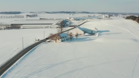 Aerial-of-farm-buildings-and-fields-covered-in-white-winter-snow-in-United-States-of-America,-USA