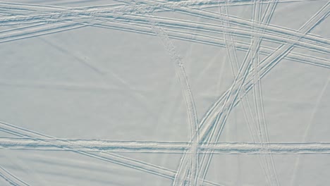 Top-down-aerial-of-snowmobile,-snow-machine-tracks-in-fresh-winter-snow-cover-in-arctic