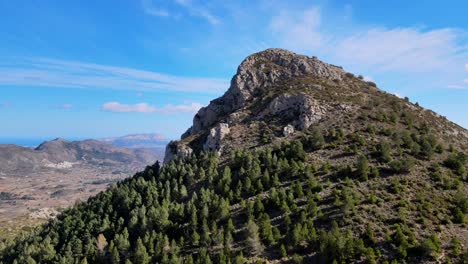 Panning-drone-footage-of-a-forested-and-rocky-mountain-Montserrat-in-Calpe,-Spain,-with-a-beautiful-blue-sky-and-cloudscape-in-the-background