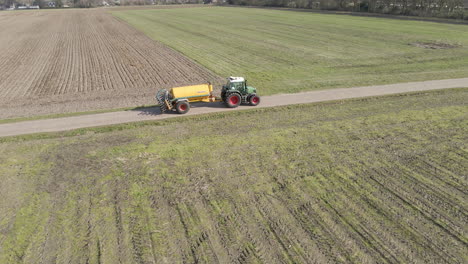 Drone-following-tractor-with-large-tank-driving-between-green-meadows