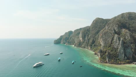 Idyllic-shoreline-coupled-by-warm-exotic-waters-hampered-by-cliff-near-Pirate-Beach-Cove,-in-Ko-Phi-Phi-Don-Island,-Thailand---Aerial-Fly-over-shot