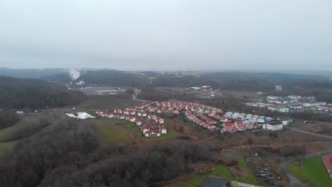 Daytime-view-small-village-with-identical-white-houses-red-rooftops-next-to-factory,-Aerial